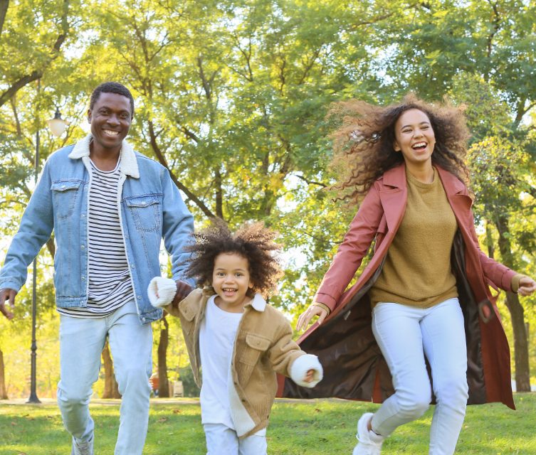 A family running hand in hand through a sunny park